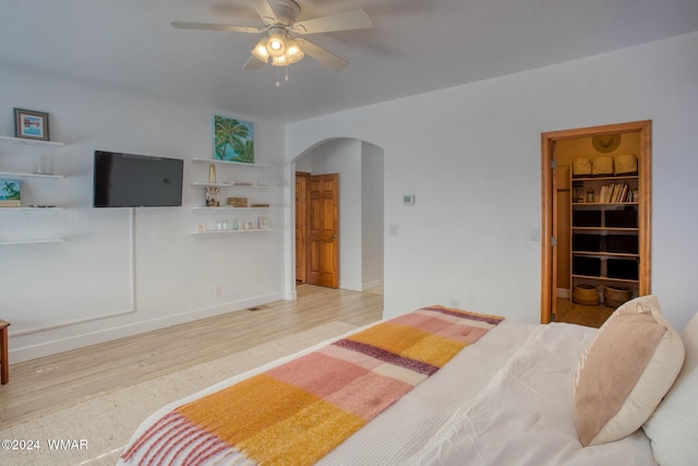 bedroom with arched walkways, baseboards, a ceiling fan, and light wood-style floors