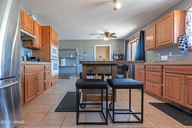 7046 Dusty Saddle Trl, Show Low, AZ 85901 - kitchen with freestanding refrigerator, wall oven, a ceiling fan, light tile patterned flooring, and white microwave