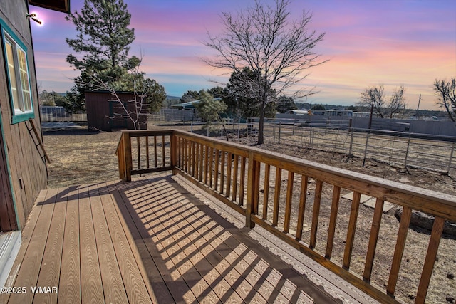 deck at dusk with a storage unit, an outdoor structure, and a fenced backyard