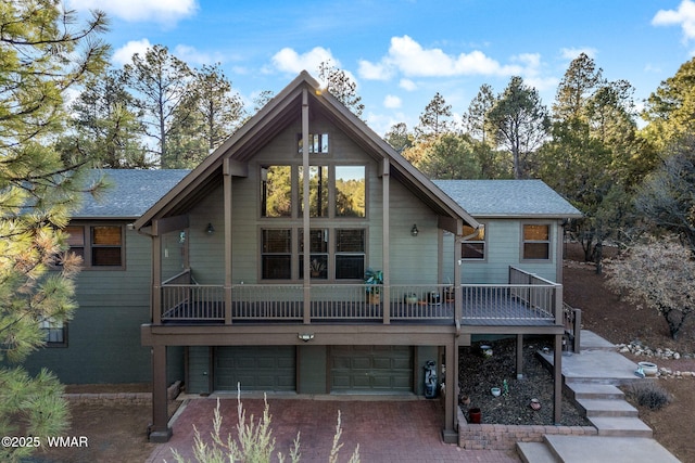 rear view of property with decorative driveway, stairway, an attached garage, and a shingled roof