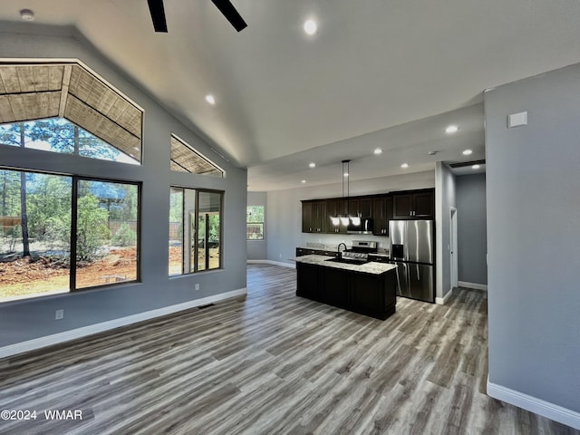 kitchen with light wood finished floors, an island with sink, open floor plan, decorative light fixtures, and stainless steel appliances