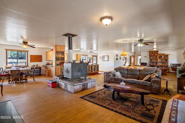 living room featuring a wood stove, a ceiling fan, and wood finished floors