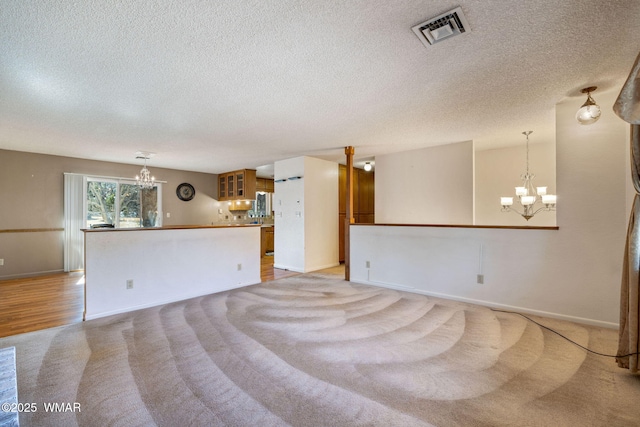 unfurnished living room with an inviting chandelier, baseboards, visible vents, and light colored carpet