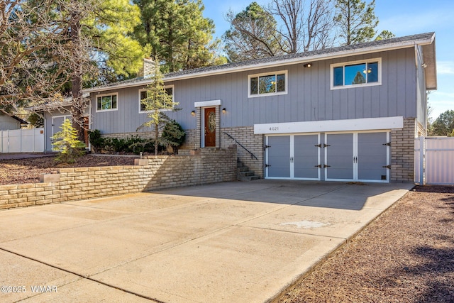 bi-level home featuring driveway, a chimney, an attached garage, fence, and brick siding