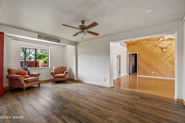 living area with dark wood-style floors, ceiling fan, baseboards, and wooden walls
