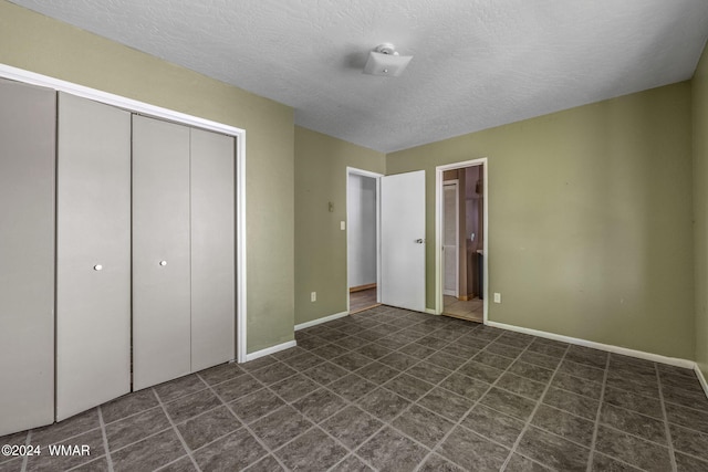 unfurnished bedroom with a textured ceiling, a closet, ensuite bath, and baseboards