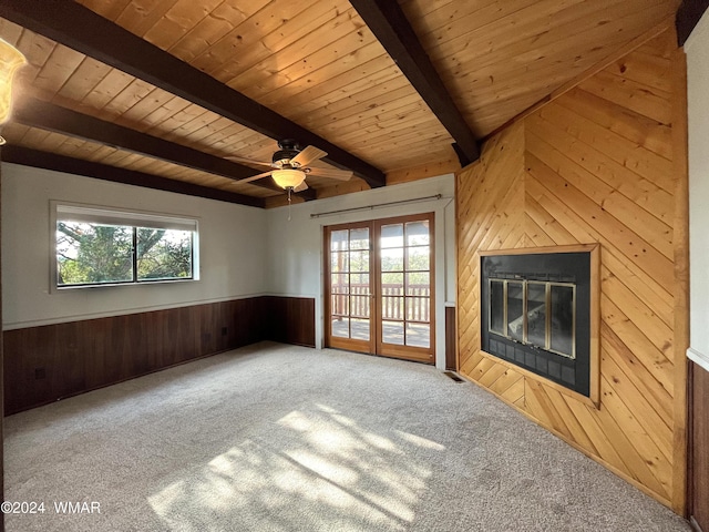 unfurnished living room with wood walls, a glass covered fireplace, a wealth of natural light, and beamed ceiling