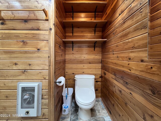 bathroom with stone finish floor, heating unit, toilet, and wooden walls