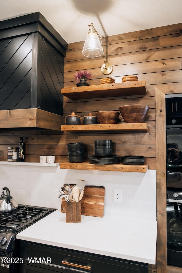 interior space featuring stainless steel gas stove, wooden walls, oven, and open shelves