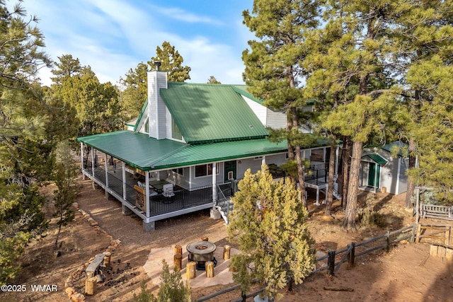 rear view of house with a fire pit, metal roof, a chimney, and fence