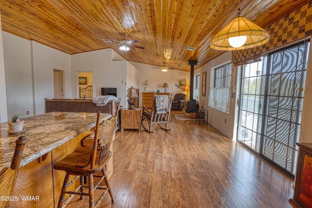 dining area featuring vaulted ceiling, wood ceiling, wood-type flooring, and a wood stove