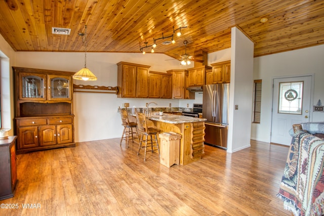 kitchen with stainless steel appliances, brown cabinetry, a breakfast bar area, and visible vents