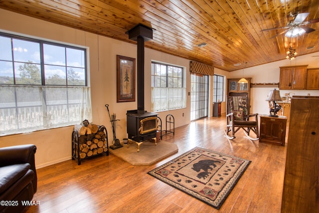 living area featuring a ceiling fan, a wood stove, vaulted ceiling, wood finished floors, and wooden ceiling