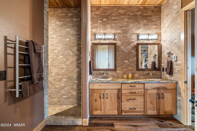 full bathroom featuring a sink, double vanity, wood finished floors, and tiled shower