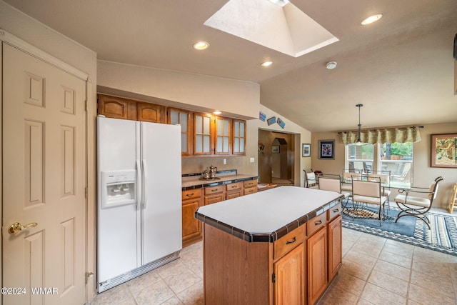 kitchen featuring brown cabinetry, a kitchen island, glass insert cabinets, white fridge with ice dispenser, and lofted ceiling with skylight