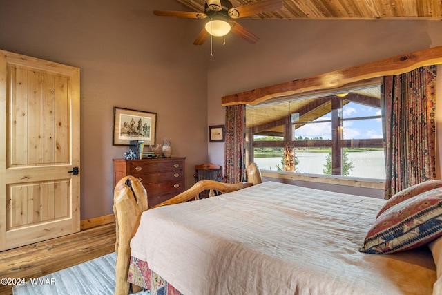 bedroom with baseboards, high vaulted ceiling, wood finished floors, and a water view