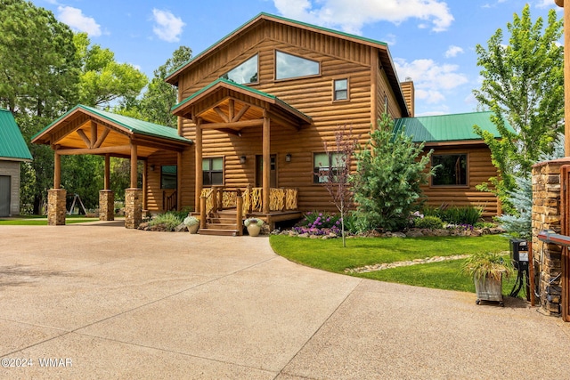 cabin with a front yard, driveway, covered porch, a chimney, and metal roof