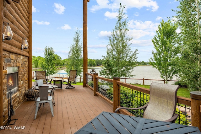 wooden terrace featuring outdoor dining space, an outdoor stone fireplace, and a water view