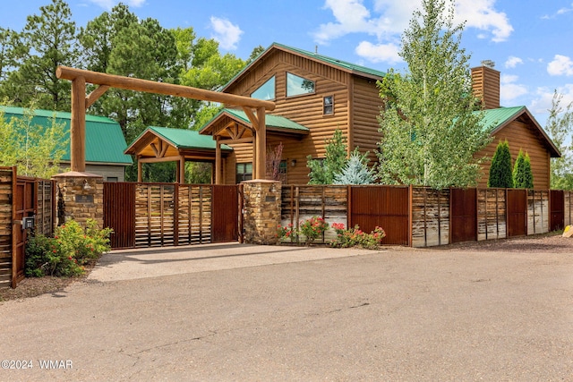 view of front facade featuring a gate, a chimney, stone siding, and metal roof