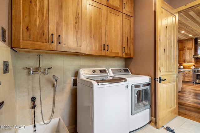 clothes washing area with cabinet space, light tile patterned floors, and washing machine and dryer