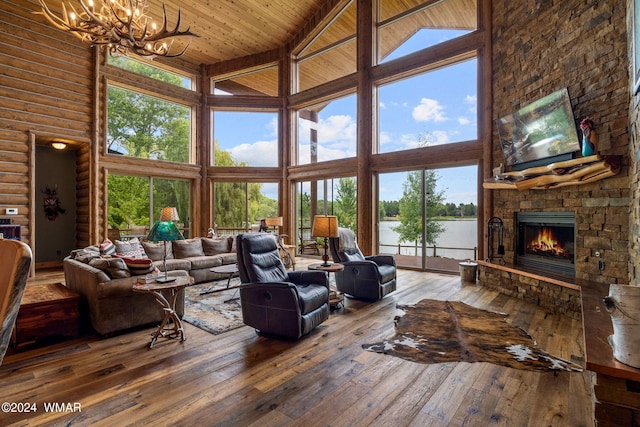 living room featuring hardwood / wood-style floors, an inviting chandelier, a stone fireplace, wooden ceiling, and rustic walls