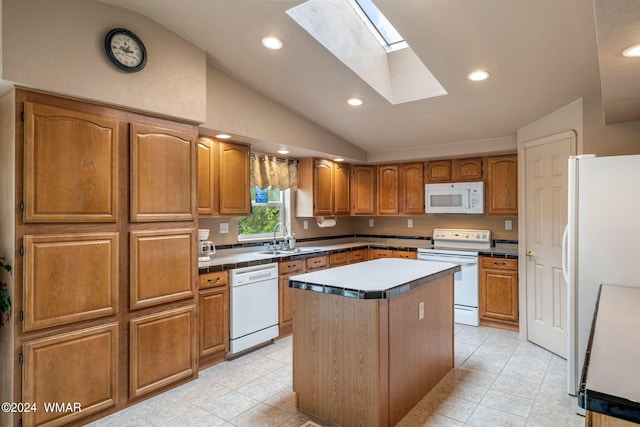 kitchen with white appliances, brown cabinetry, vaulted ceiling with skylight, a sink, and a center island