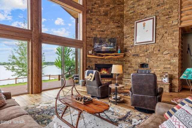 living room with a wealth of natural light, a stone fireplace, a towering ceiling, and wood finished floors