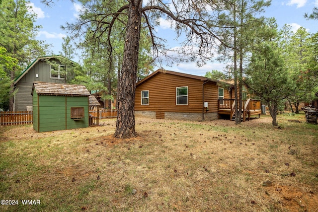 rear view of property featuring a deck, an outdoor structure, fence, and a shed