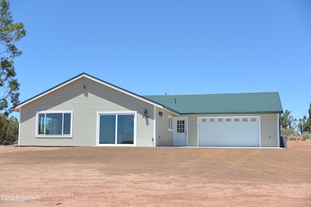 ranch-style house featuring a garage, metal roof, and dirt driveway