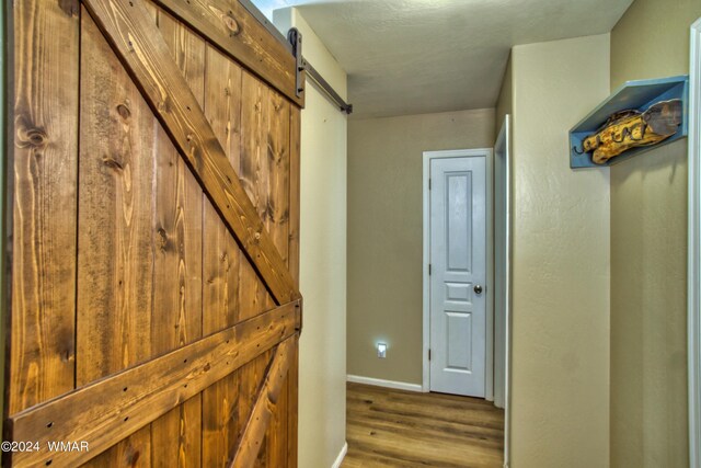 hallway with baseboards, a barn door, and wood finished floors