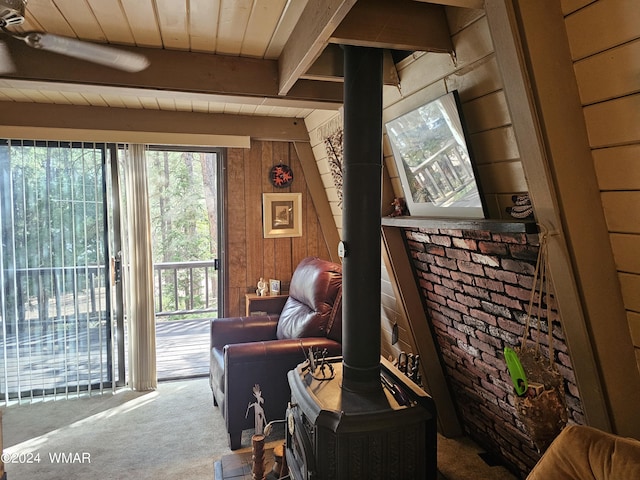 sitting room featuring a wood stove, carpet flooring, wooden walls, wooden ceiling, and beamed ceiling