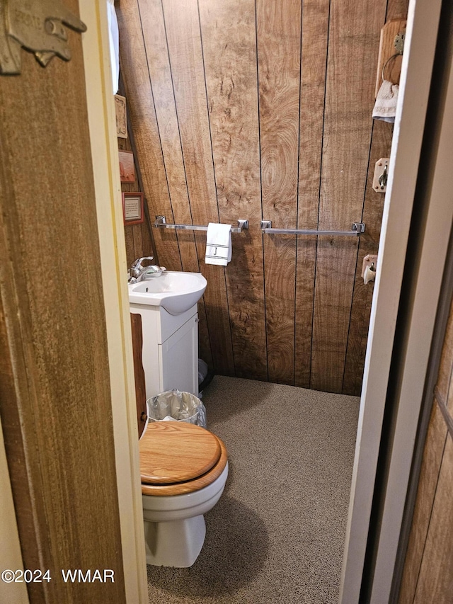 half bathroom featuring toilet, wood walls, and vanity