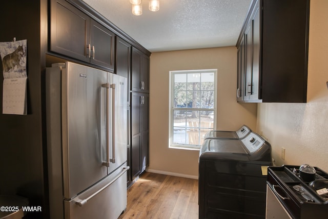 laundry area with laundry area, a textured ceiling, washing machine and clothes dryer, light wood-type flooring, and baseboards