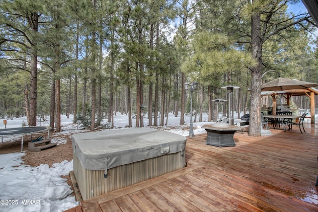snow covered deck with an outdoor fire pit, a gazebo, a trampoline, a hot tub, and outdoor dining space