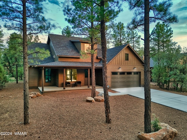 view of front of house with roof with shingles, a porch, concrete driveway, board and batten siding, and a garage