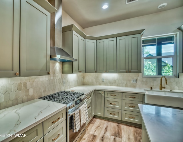 kitchen with visible vents, wall chimney exhaust hood, backsplash, a sink, and gas stove