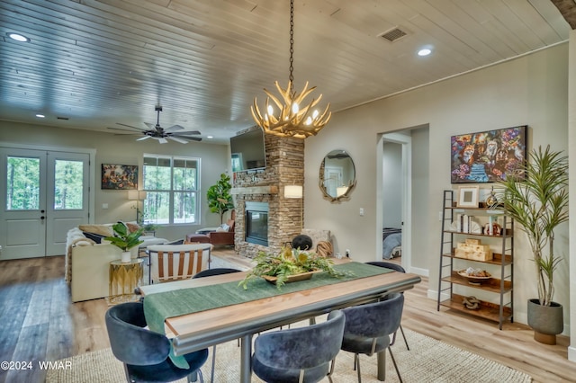 dining space with light wood finished floors, a stone fireplace, wooden ceiling, and visible vents