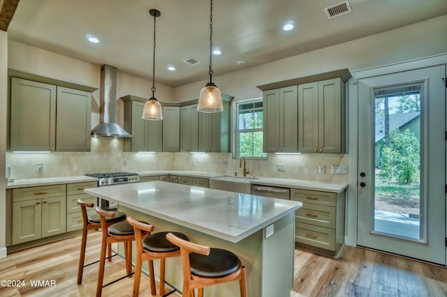 kitchen featuring wall chimney exhaust hood, hanging light fixtures, a breakfast bar area, and visible vents