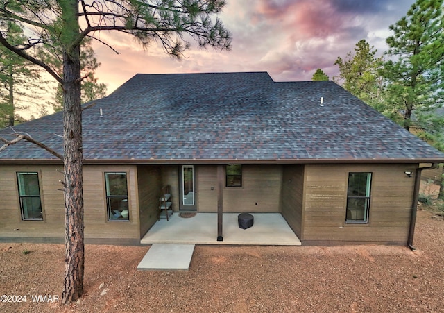 back of property at dusk with a shingled roof and a patio