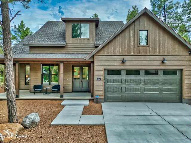 view of front of property with covered porch, a garage, driveway, french doors, and roof with shingles