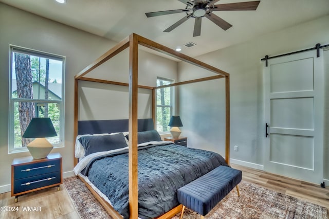 bedroom with light wood-style floors, a barn door, multiple windows, and visible vents