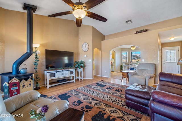 living room featuring arched walkways, ceiling fan, visible vents, light wood-type flooring, and a wood stove