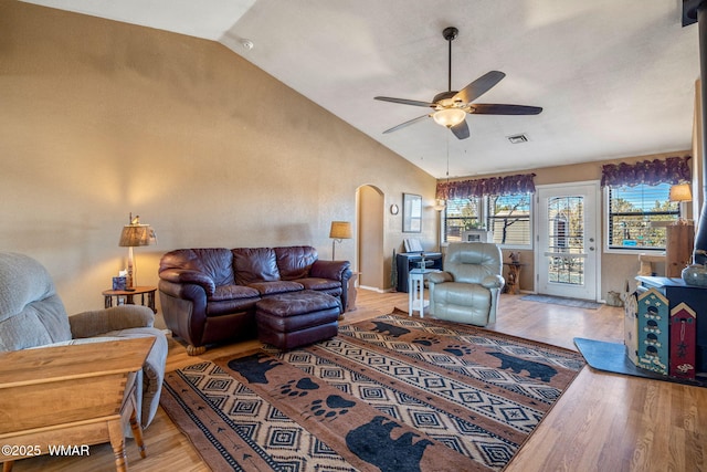 living area with visible vents, arched walkways, light wood-style flooring, ceiling fan, and high vaulted ceiling