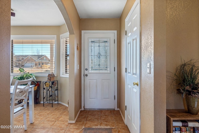 foyer entrance featuring arched walkways, a textured wall, light tile patterned floors, and baseboards