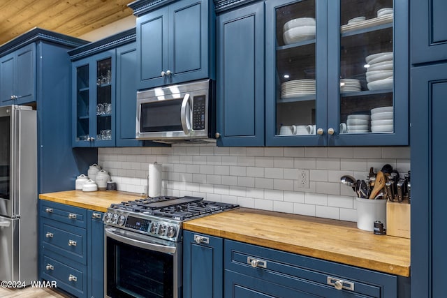 kitchen with blue cabinets, butcher block counters, appliances with stainless steel finishes, and glass insert cabinets