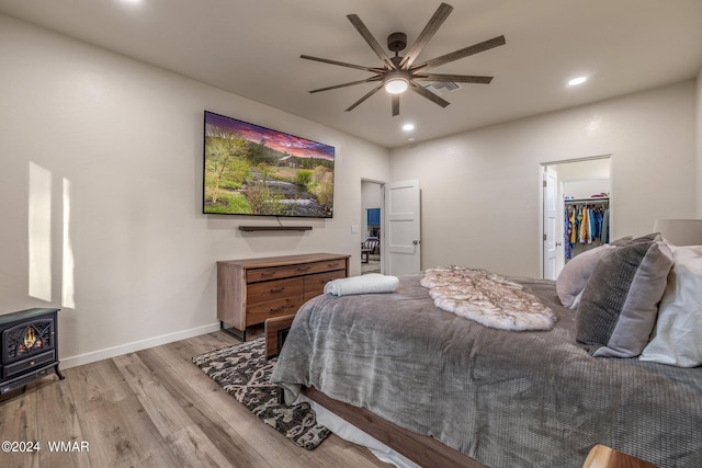 bedroom featuring recessed lighting, light wood-style flooring, a spacious closet, a wood stove, and baseboards