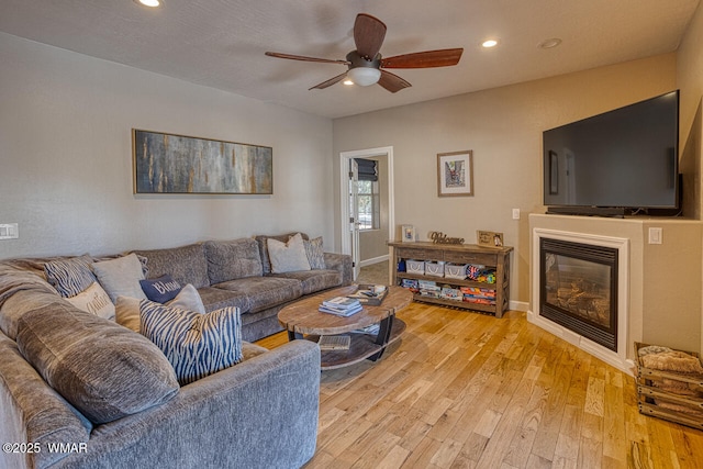 living room featuring baseboards, light wood-style flooring, recessed lighting, ceiling fan, and a glass covered fireplace