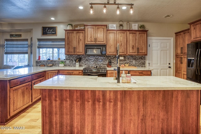 kitchen with visible vents, black appliances, a center island with sink, light wood-style flooring, and backsplash