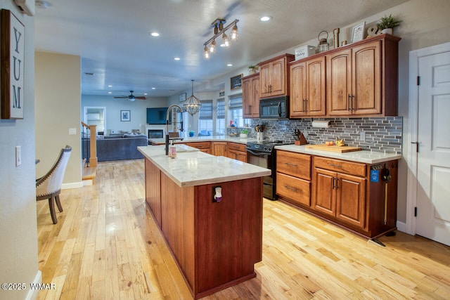 kitchen featuring light wood-type flooring, black appliances, light countertops, open floor plan, and tasteful backsplash