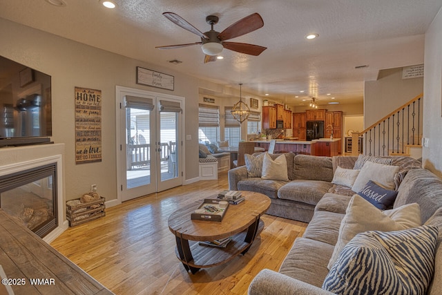 living room with recessed lighting, stairs, light wood-style floors, a textured ceiling, and ceiling fan with notable chandelier